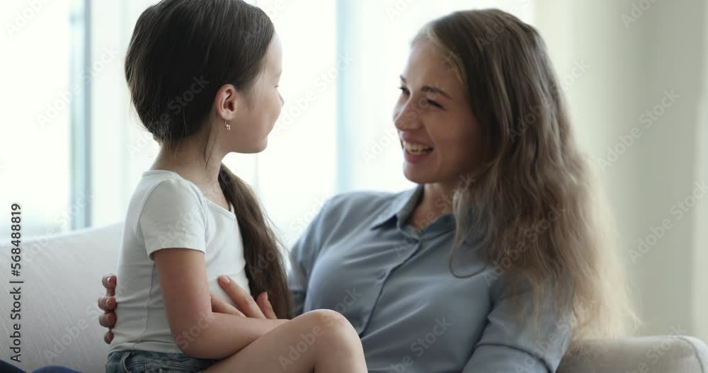 Close up of beautiful loving mother play with adorable cute little daughter seated together on sofa, tickling, laughing, enjoy funny playtime on weekend at home. Happy motherhood, custody, family bond Close up of beautiful loving mother play with adorable cute little daughter seated together on sofa, tickling, laughing, enjoy funny playtime on weekend at home. Happy motherhood, custody, family bond