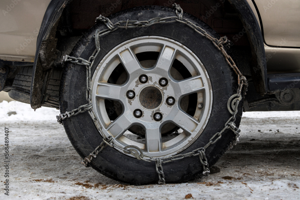 Wheel Car with winter chains for snow and ice road . Snow chains on tire. The wheel of a car with snow chain Wheel Car with winter chains for snow and ice road . Snow chains on tire. The wheel of a car with snow chain