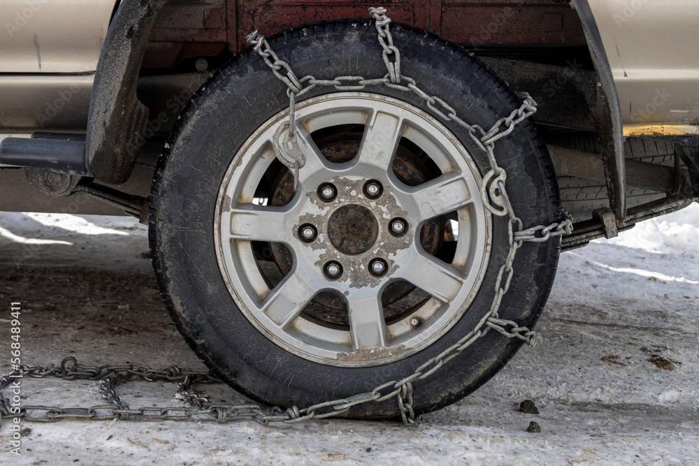 Wheel Car with winter chains for snow and ice road . Snow chains on tire. The wheel of a car with snow chain Wheel Car with winter chains for snow and ice road . Snow chains on tire. The wheel of a car with snow chain
