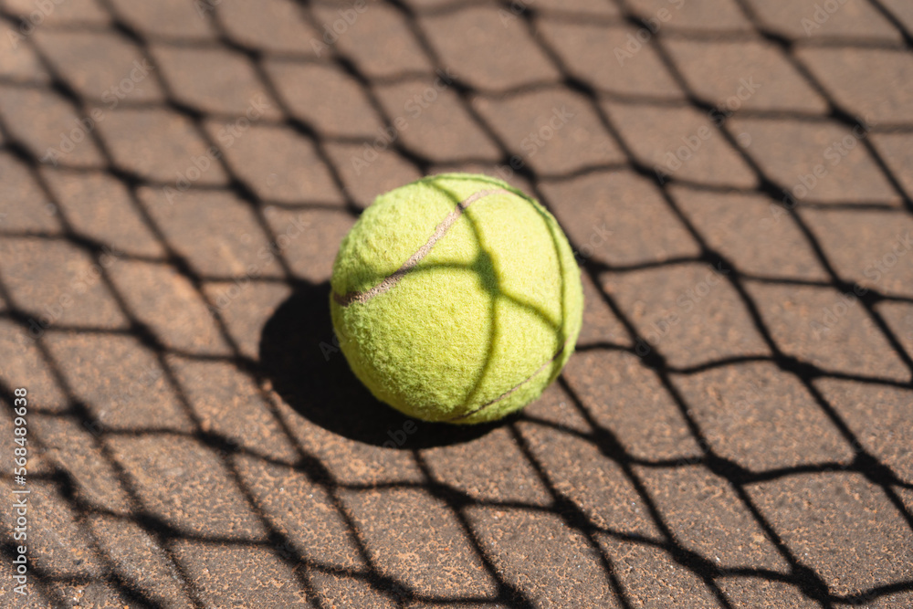 Top view of yellow tennis ball placed on court and covered with shadow of net on sunny day