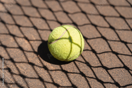 Top view of yellow tennis ball placed on court and covered with shadow of net on sunny day © diignat