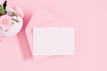 Top view on open pink envelope with paper card, bouquet of pink flowers rose on pastel pink table background. Birthday, Wedding, Mother's Day, Valentine's day, Women's Day. Flat lay, copy space