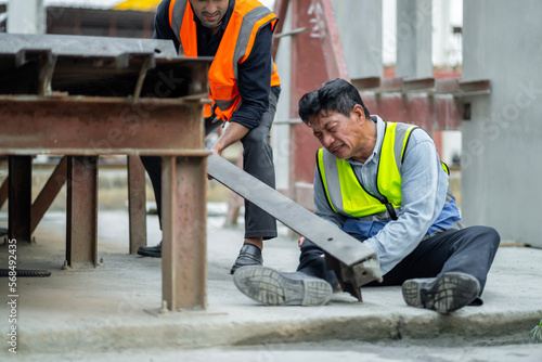 An engineer has an accident where steel falls on his leg at work, causing serious leg injuries. and get help from colleagues in the area under construction industrial factory, concept, safe work