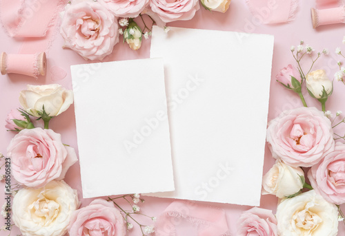 Blank paper cards between pink roses and pink silk ribbons on pink top view, wedding mockup