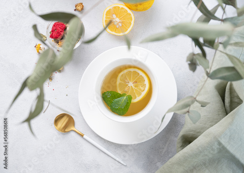 Herbal tea with lemon and mint in a white cup on a light background with eucalyptus branches. The concept of a healthy and delicious drink for immunity.