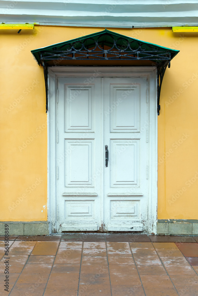 Fototapeta premium Old white wooden door with a canopy on the yellow wall