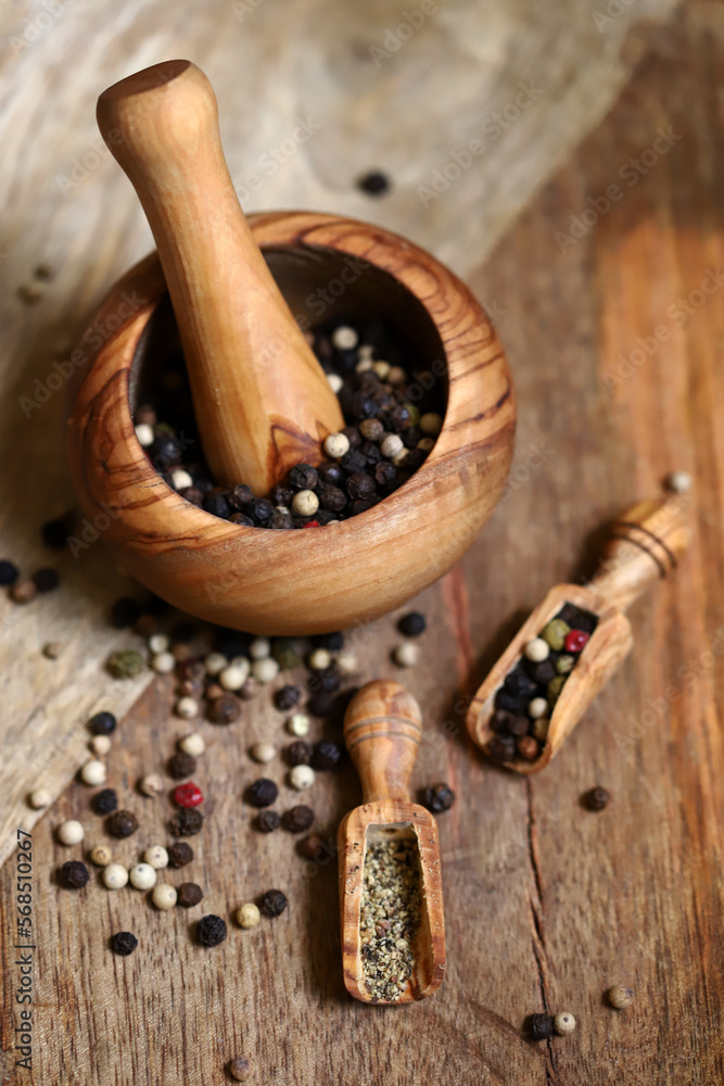 Mix of peppercorns in a wooden mortar and wooden spatulas.