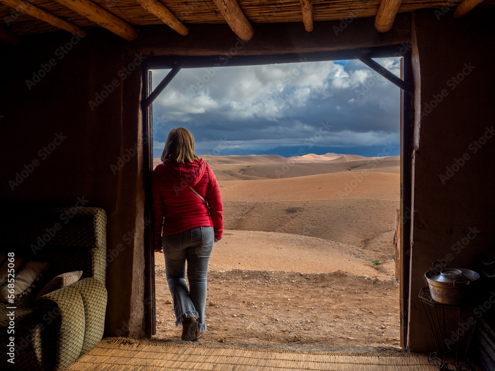 Woman next to the door of a Moroccan adobe house looking at the desert