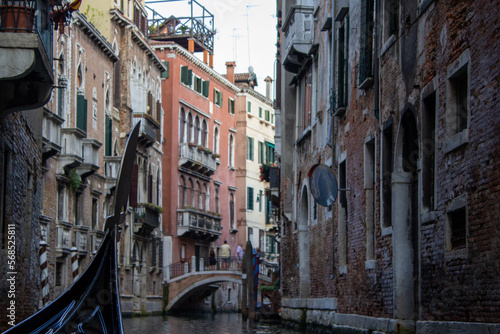 View from a gondola gliding through a quiet Venetian canal, flanked by historic weathered buildings and a footbridge, capturing the essence of Venice's charming waterways.