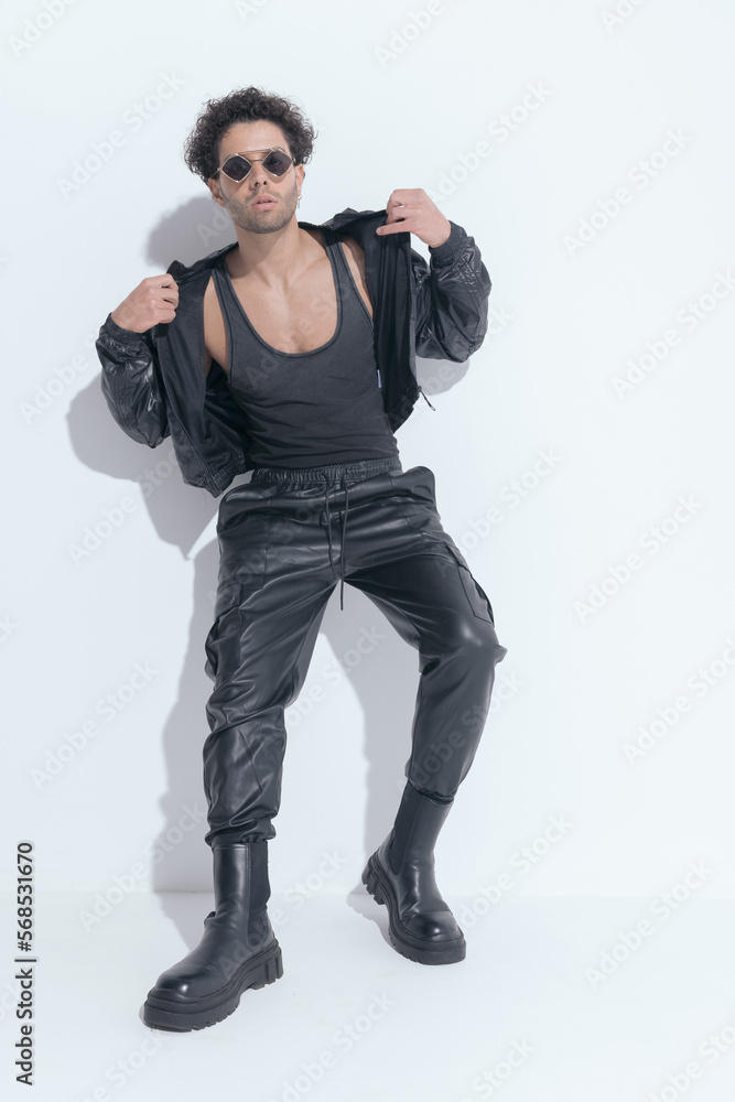 sexy greek guy with curly hair adjusting leather jacket while laying on a wall sexy greek guy with curly hair adjusting leather jacket while laying on a wall