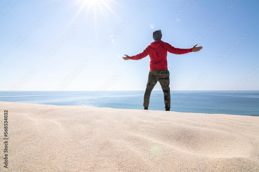Mature man, over fifty years old. Meditating on the sand dunes. The dunes, the sea, the blue sky and the sun as a background. Mature man, over fifty years old. Meditating on the sand dunes. The dunes, the sea, the blue sky and the sun as a background.