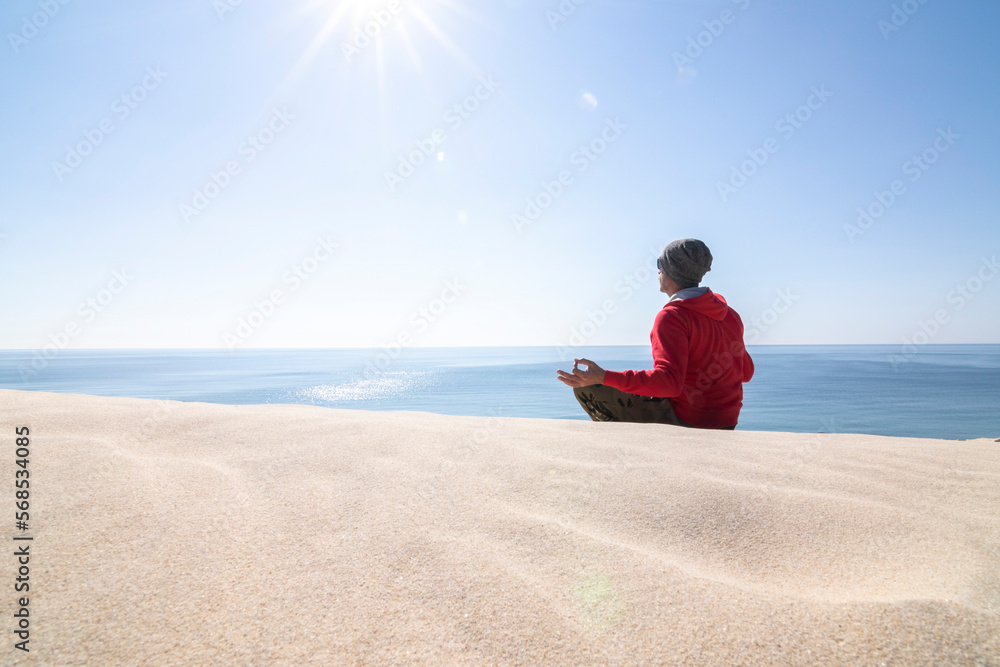 Mature man, over fifty years old. Meditating on the sand dunes. The dunes, the sea, the blue sky and the sun as a background.