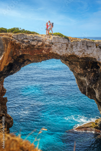 Ein verliebtes Paar läuft auf einer Felsbrücke über einer Bucht bzw. Grotte, Pont natural d'Es Caló Blanc, Mallorca, Balearen, Spanien, Europa photo