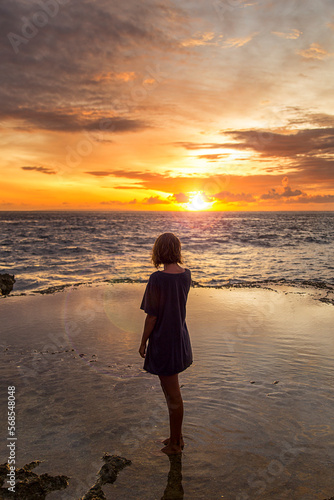 Woman with her back to the camera, watching the sun set in the sea. Travel and pleasure. © FEDEMARINIC