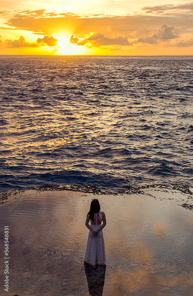Woman with her back to the camera, watching the sun set in the sea. Travel and pleasure.