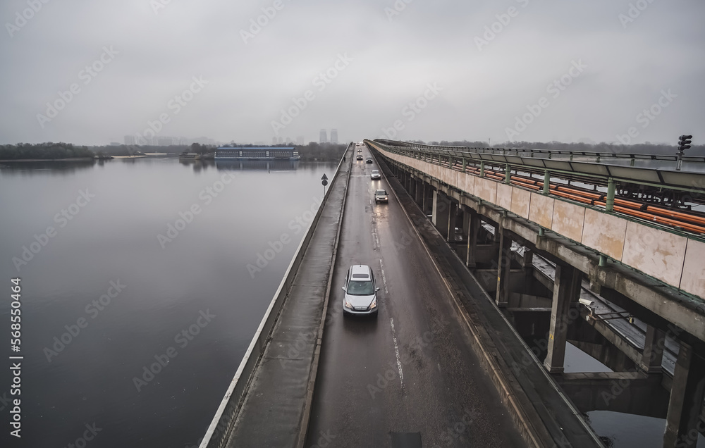 Automobile and railway bridge over the Dnieper river in Kyiv with cars, cloudy day in spring