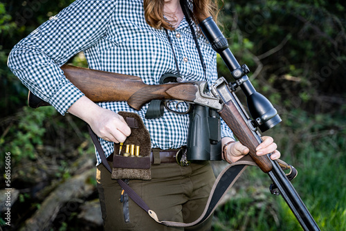 Junge Jägerin hat ihre Flinte mit Zielfernrohr, Fernglas und Munitionstasche bei der Jagd dabei. photo