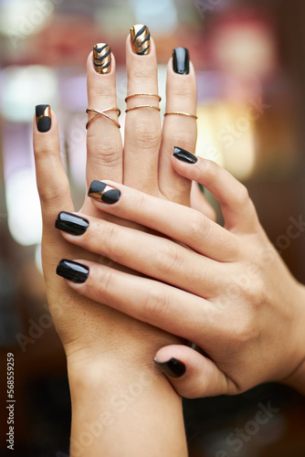 black and gold manicure, hands on a blurred background. Close-up hands of a young woman with a black-gold manicure with rings on her fingers