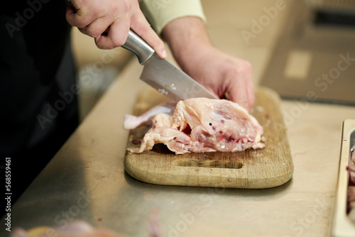 chef cuts chicken meat with a kitchen axe. hands cut chicken meat into pieces. The butcher cuts a chicken carcass with a kitchen ax on a cutting board for cooking.