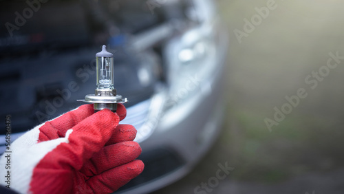The hand of the master holds a halogen light bulb against the background of the car.Replacing the light bulb in the car.Replacement of lighting. photo