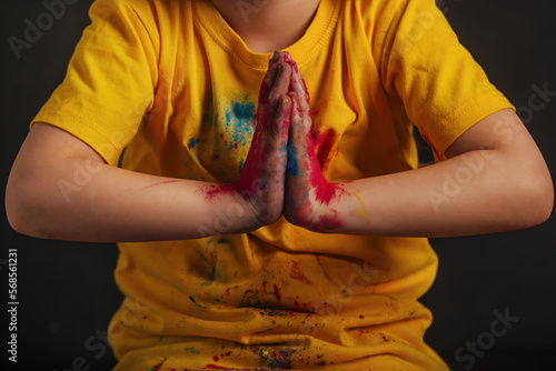 children's hands in bright multi-colored Holi colors are folded in a Namaste greeting gesture. Meet the Indian festival Holi