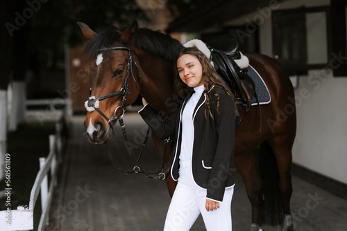Beautiful professional female jockey standing near horse. woman horse rider is preparing to equitation. girl and horse. equestrian sport concept. riding vacation. friendship with horse