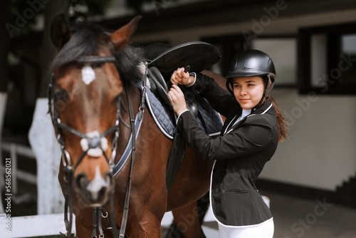 Girl rider adjusts saddle on her horse to take part in horse races.
