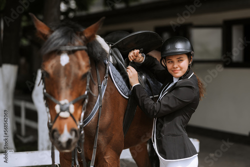 Girl rider adjusts saddle on her horse to take part in horse races. © JJ Studio