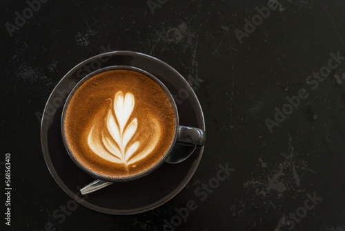 Obraz na płótnie Hot coffee latte with latte art milk foam in cup mug on black wood desk on top view. As breakfast In a coffee shop at the cafe,during business work concept w salonie