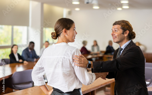 Positive young woman shaking hand of businessman employer during meeting in company office.
