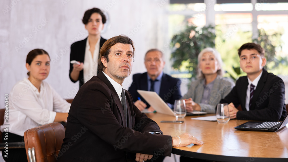 Focused businessman sitting at table in office, listening attentively to presentation of partners during meeting