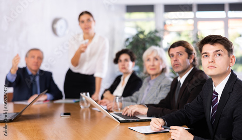 Woman and man sitting at table beside her colleagues during meeting in conference room
