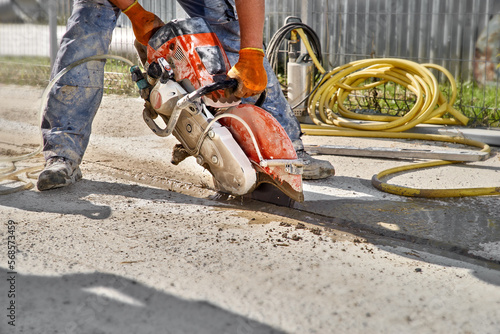 Construction worker cutting concrete foundation using a cut-off saw. Profile on the blade of an asphalt or concrete cutter with workers shoes and protective gear photo