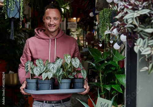 Portrait of man holding tray of plants in doorway of flower shop