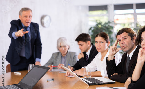 Angry male boss reprehending colleagues on meeting in modern office