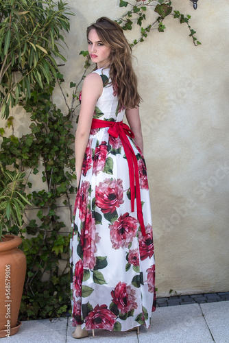 Girl in a summer dress stands next to a flower wall