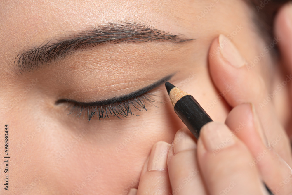 woman applying cosmetic pencil on eye
