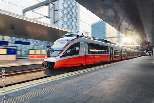 Red high speed train in motion on the railway station at sunset. Fast modern intercity train and blurred background. Railway platform. Railroad in Austria. Commercial and passenger transportation