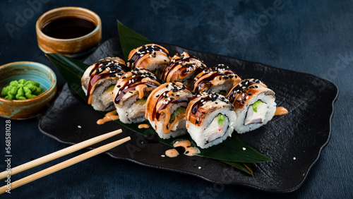 Japanese sushi rolls with smoked eel, shrimps, cream cheese, avocado, soy sauce, wasabi and chopsticks.