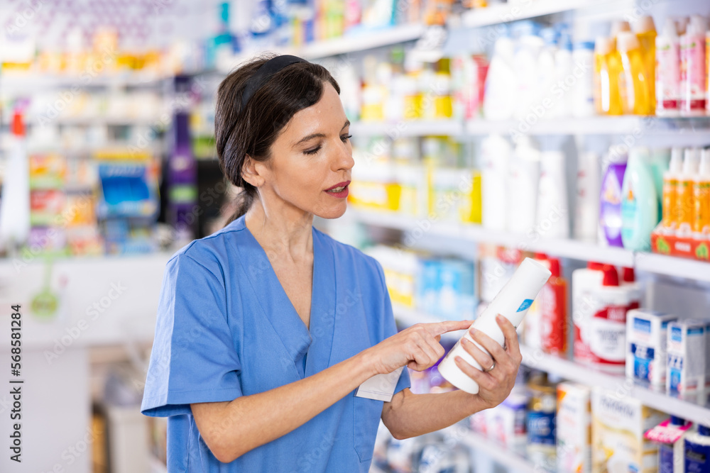 Portrait of positive female pharmacist advising consumer in drug store, showing product