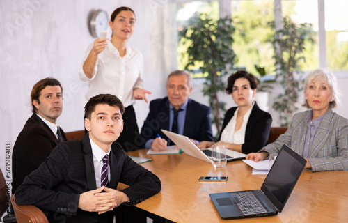 Portrait of young office worker sitting at table with colleagues, listening with interest and watching presentation during business meeting