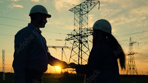 Team of power engineers builders, woman, man, are working together on repair of electrical high voltage pylons. Teamwork energy engineers working together outdoors. Electricians in safety helmet