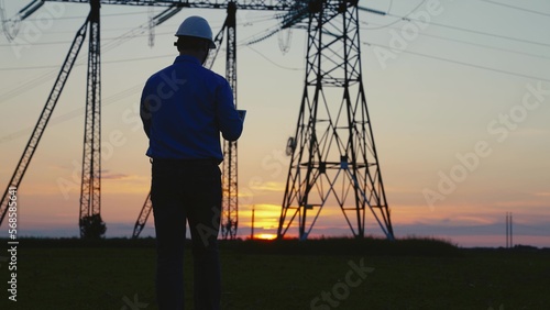Silhouette of an engineer builder power engineer in a helmet checks the power line using a computer on a tablet. Repair, maintenance and construction of high voltage electrical lines. Green energy