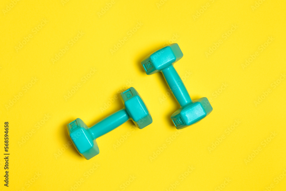 Two bright blue or mint dumbbells are isolated on yellow background. Sport and health concept. Two bright blue or mint dumbbells are isolated on yellow background. Sport and health concept.
