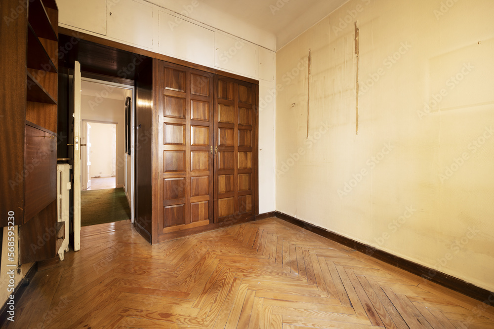 Obraz premium An old and empty bedroom with a built in wardrobe with two folding doors with dark wooden paneling