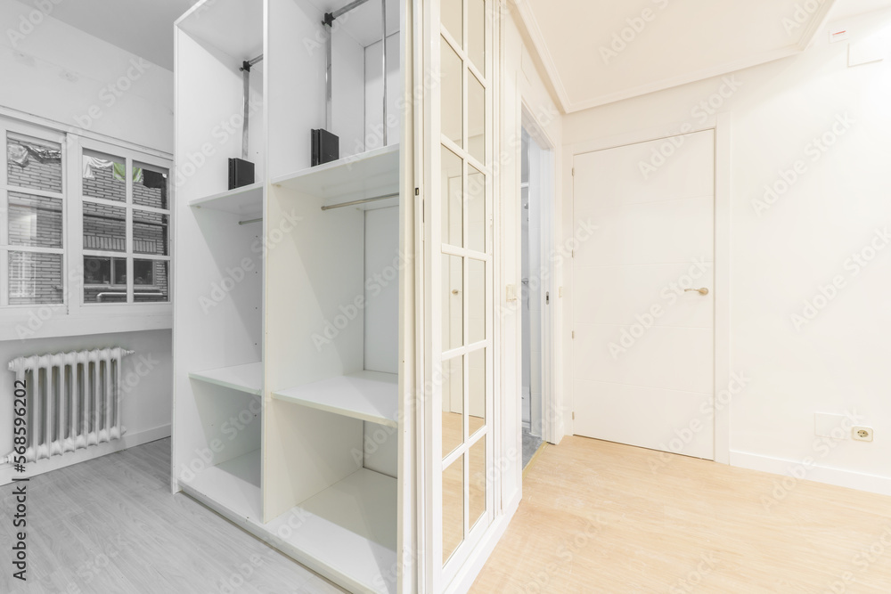 A bedroom dressing room with white and mirror aluminum sliding doors and many shelves