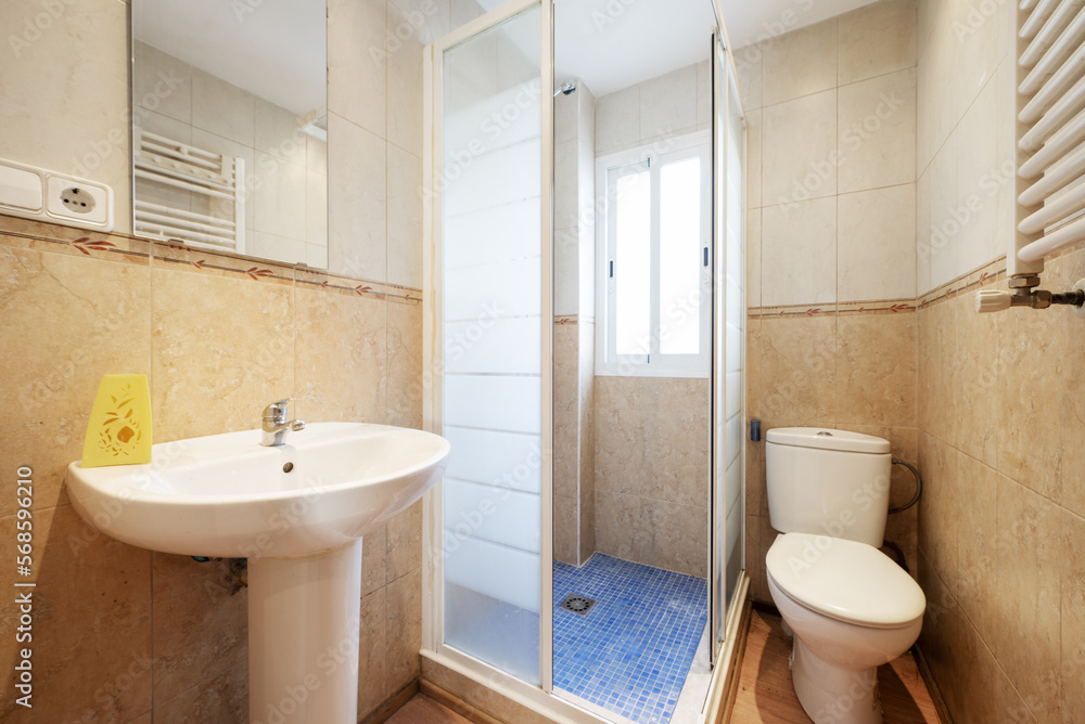 WC with white porcelain sink under a mirror embedded in the wall of a studio and sliding shower cubicle with a window inside WC with white porcelain sink under a mirror embedded in the wall of a studio and sliding shower cubicle with a window inside