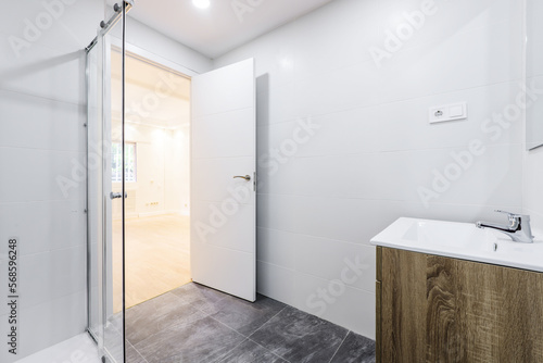 bathroom with wooden sink below frameless wall-hung mirror, walk-in shower with screens