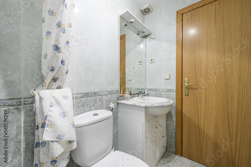 Bathroom with white furniture, mirror with sconces, oak wood door and two-tone tiles with a border