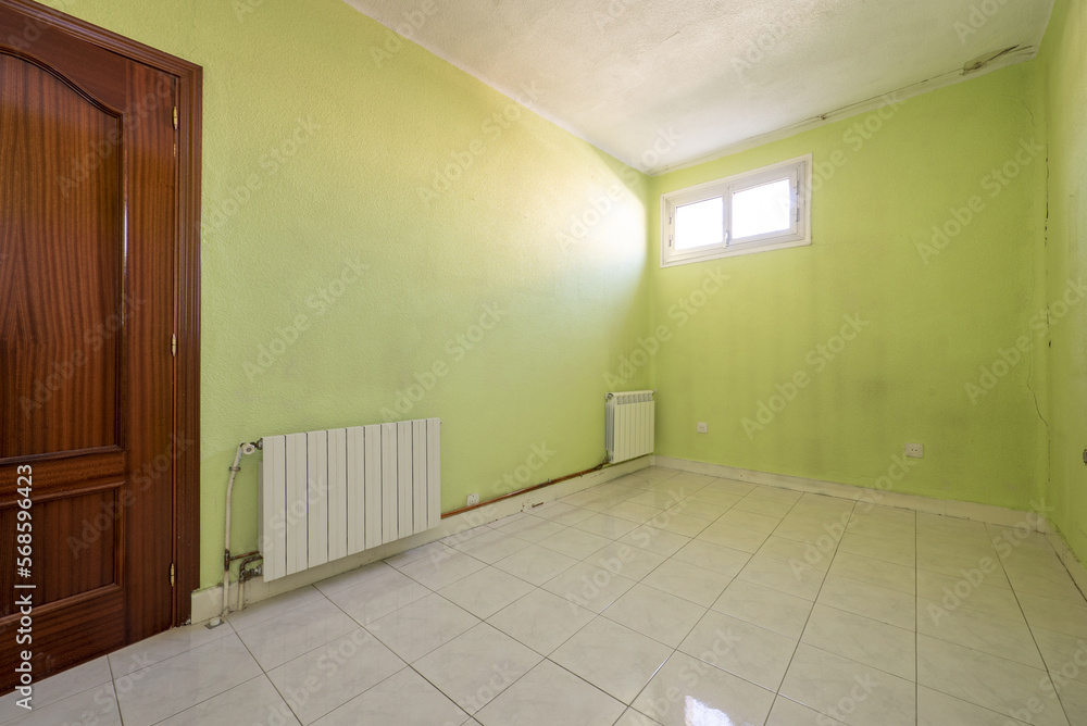 Empty room with two radiators, green painted walls, small windows on the wall, glossy stoneware floors and a sapele door Empty room with two radiators, green painted walls, small windows on the wall, glossy stoneware floors and a sapele door